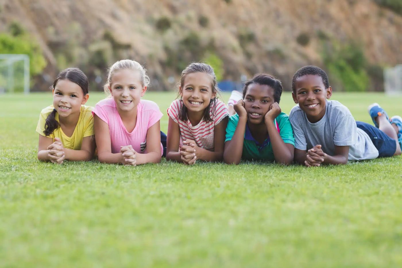 Vijf basisschoolkinderen liggen naast elkaar in het gras